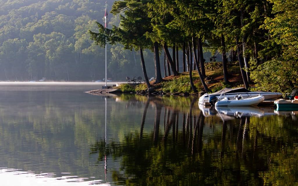 Morning mist breaks over the glassy still Lake Joseph.